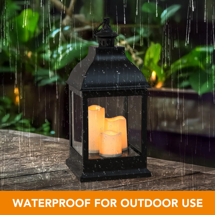 Black lantern with candles on a wooden surface outdoors, surrounded by greenery.