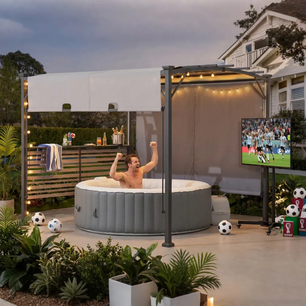 Man in a hot tub watching sports on TV with soccer balls and drinks around