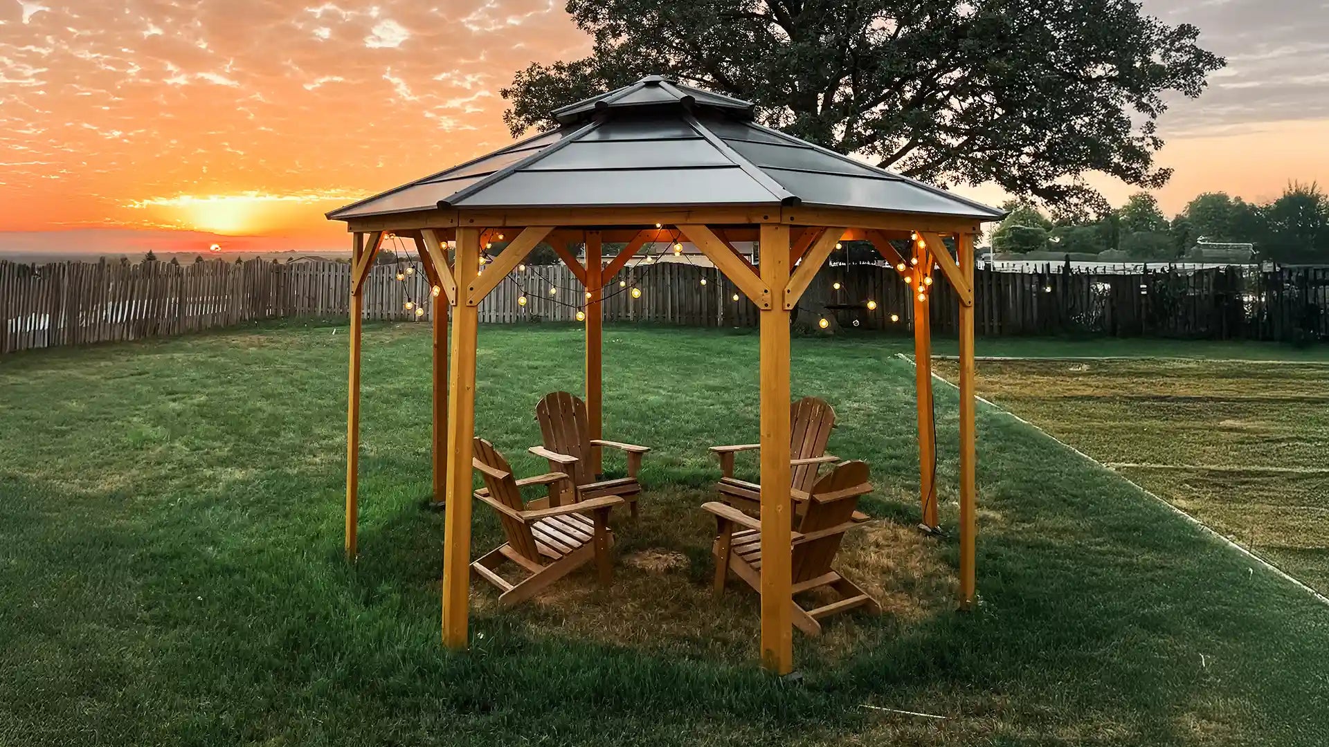 Wooden gazebo with chairs on a grassy area during sunset.